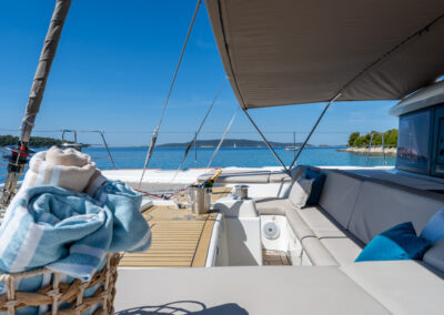 A stunning view of the Lagoon 560 catamaran's spacious front deck. The deck features comfortable seating area with a small table. In the background, you can see a breathtaking view of the Croatian coastline and crystal-clear waters.