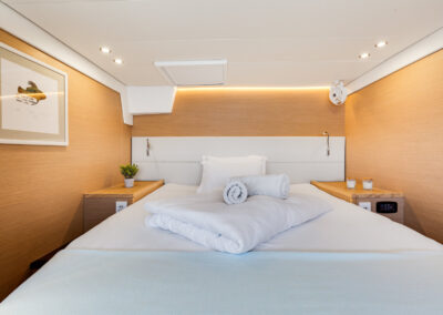 A luxurious bedroom on the Lagoon 560 s2 catamaran, with a king-size bed, wooden furnishings and a small ceiling fan.