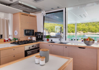 A modern and well-equipped kitchen on the Lagoon 560 catamaran. The galley features stainless steel appliances, ample counter space, and large windows offering stunning sea views.