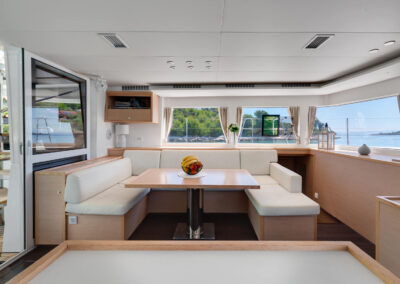 A spacious and modern interior of the Lagoon 560 catamaran. The salon features comfortable seating, a dining table, and large windows offering stunning sea views.