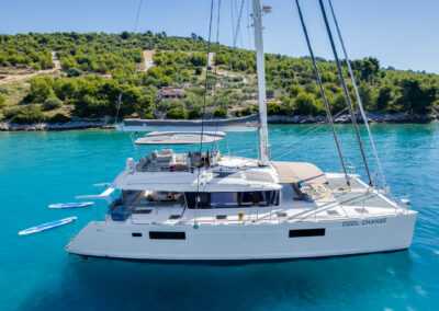 A side areal view of the luxurious Lagoon 560 catamaran, anchored in a secluded bay on the Croatian coast. The crystal-clear waters, lush green islands, and the elegant design of the yacht create a picture-perfect scene for a dream vacation.