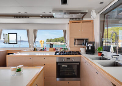 A modern and well-equipped kitchen on the Lagoon 560 catamaran. The galley features stainless steel appliances, ample counter space, and large windows offering stunning sea views.