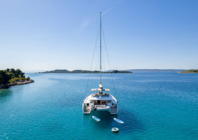 A stunning rear aerial view of the Lagoon 560 catamaran. The catamaran's impressive sail and spacious deck are showcased, along with paddleboards floating nearby.