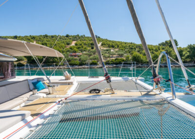 A stunning view of the Lagoon 560 catamaran's spacious sunbathing net. The catamaran is anchored in a serene bay, with lush green hills in the background.