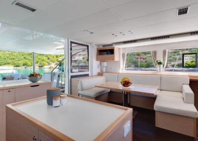 A spacious and modern interior of the Lagoon 560 catamaran. The salon features comfortable seating, a dining table, and large windows offering stunning sea views.