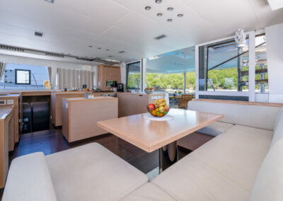 A spacious and modern interior of the Lagoon 560 catamaran. The salon features comfortable seating, a dining table, and large windows offering stunning sea views. The well-equipped galley is perfect for preparing delicious meals.