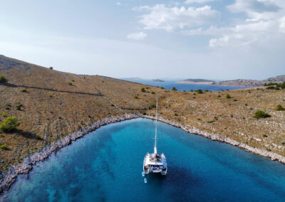 A stunning aerial view of a Lagoon 560 catamaran anchored in a secluded bay on the Croatian coast. The crystal-clear waters, rocky islands.