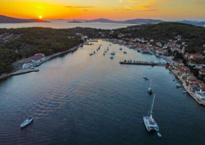 A breathtaking sunset aerial view of the Cool Change, a Lagoon 560 catamaran, anchored in a picturesque harbor on a Croatian island.