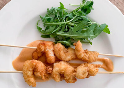 A plate of delicious crispy shrimp skewers served with a creamy sauce and a side of fresh arugula.