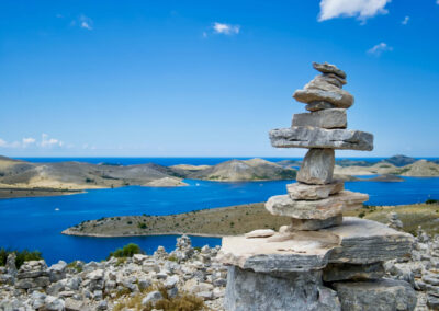 A stunning view of the Kornati Islands in Croatia, featuring a traditional stone cairn in the foreground. The clear blue sea, dotted with small islands, stretches out into the distance.