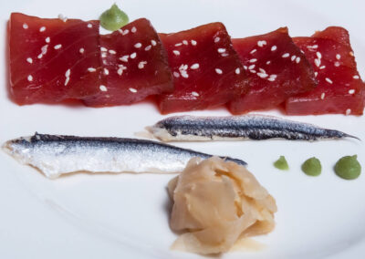 A close-up of a plate of fresh tuna sashimi, garnished with sesame seeds, pickled anchovies, ginger, and wasabi. This delicious dish is prepared by our talented onboard chef and is just one of the many culinary delights you can experience on the Lagoon 560 catamaran.