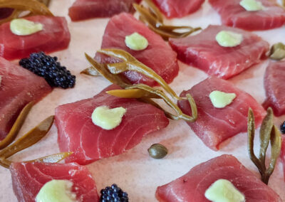 A close-up of a plate of delicious tuna carpaccio, garnished with seaweed, caviar, and a creamy sauce. This gourmet dish is just one of the many culinary delights you can enjoy on board the Lagoon 560 catamaran.