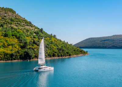 A stunning view of the Cool Change, a Lagoon 560 catamaran, sailing through a crystal-clear blue bay in Croatia.