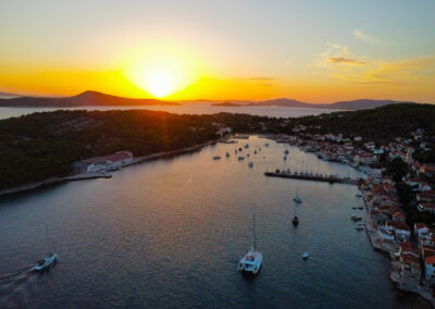 A breathtaking sunset aerial view of the Cool Change, a Lagoon 560 catamaran, anchored in a picturesque harbor on a Croatian island.