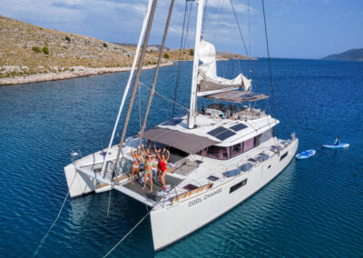 A happy group of women waving to the drone camera on the spacious net of the Cool Change, a Lagoon 560 catamaran, during their luxury yacht charter in Croatia.