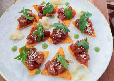 A plate of tuna tartare served on crispy tortilla chips with arugula and sesame seeds.